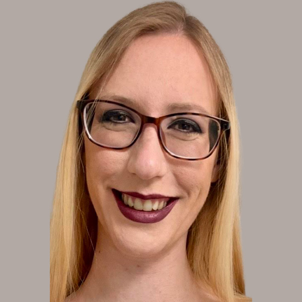 A blonde woman with glasses against a gray background.